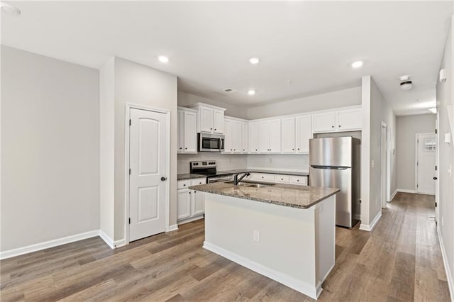 kitchen with white cabinets, an island with sink, appliances with stainless steel finishes, wood finished floors, and a sink