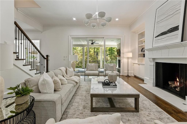 living room with light hardwood / wood-style floors, an inviting chandelier, ornamental molding, and built in shelves