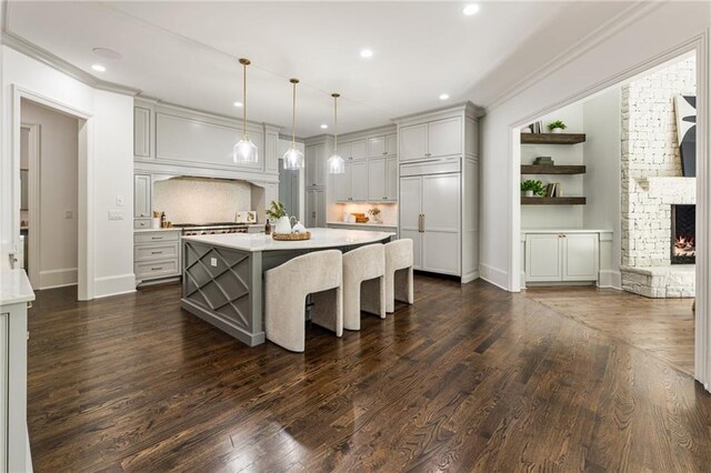 kitchen with dark wood-type flooring, a stone fireplace, a center island, and hanging light fixtures