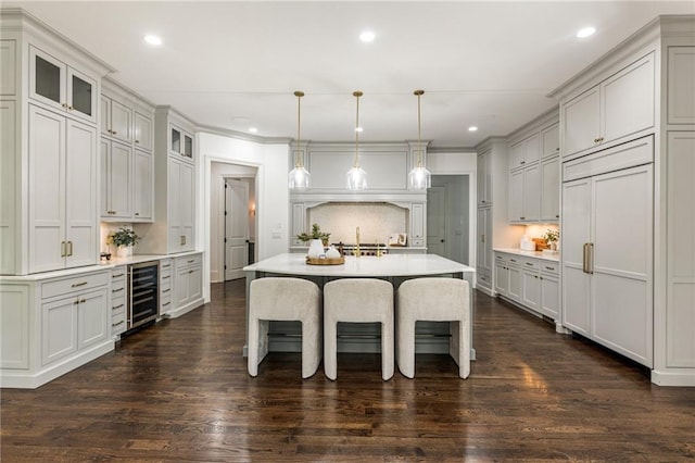 kitchen with wine cooler, a kitchen island with sink, decorative light fixtures, and dark hardwood / wood-style floors