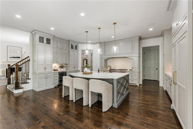 kitchen featuring an island with sink, dark hardwood / wood-style flooring, white cabinetry, pendant lighting, and crown molding