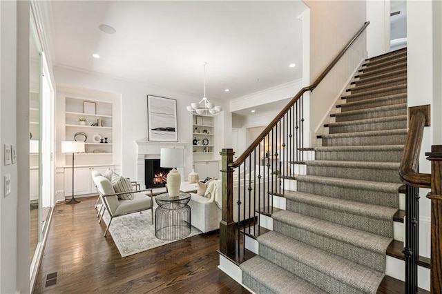 living room with crown molding, a chandelier, built in shelves, and dark hardwood / wood-style flooring