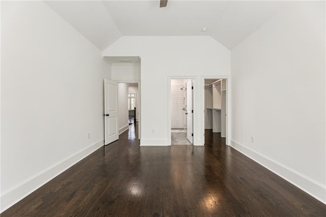 unfurnished bedroom with vaulted ceiling, a walk in closet, a closet, and dark hardwood / wood-style flooring