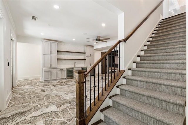 stairway featuring ceiling fan, crown molding, beverage cooler, and wet bar