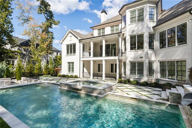 rear view of property with a balcony, a patio, and a pool with hot tub