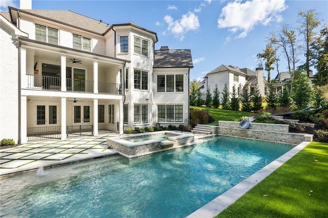 rear view of house with a yard, a balcony, a swimming pool with hot tub, a patio, and ceiling fan