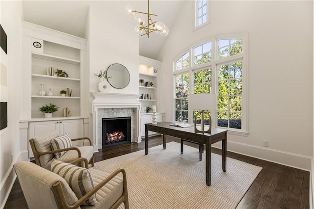 office space featuring high vaulted ceiling, dark hardwood / wood-style flooring, a high end fireplace, a notable chandelier, and built in shelves