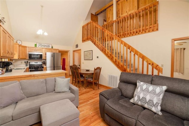 living room featuring visible vents, high vaulted ceiling, stairs, light wood-style floors, and a chandelier