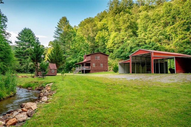 view of yard featuring a forest view, a detached carport, an outdoor structure, and driveway