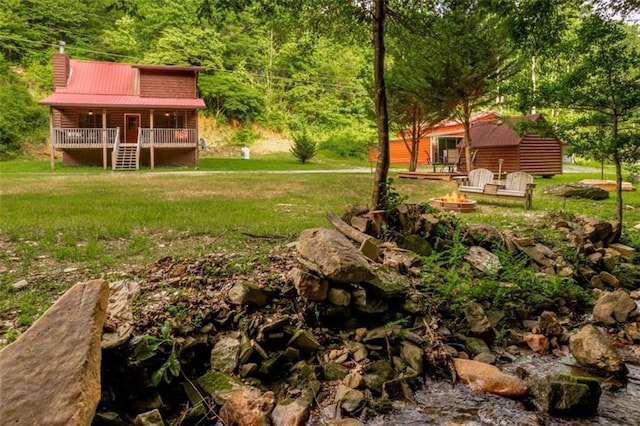 view of yard featuring a forest view, a porch, and an outdoor fire pit