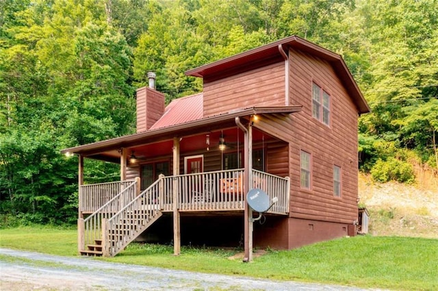 view of front of house featuring a wooded view, a front lawn, stairs, a chimney, and metal roof