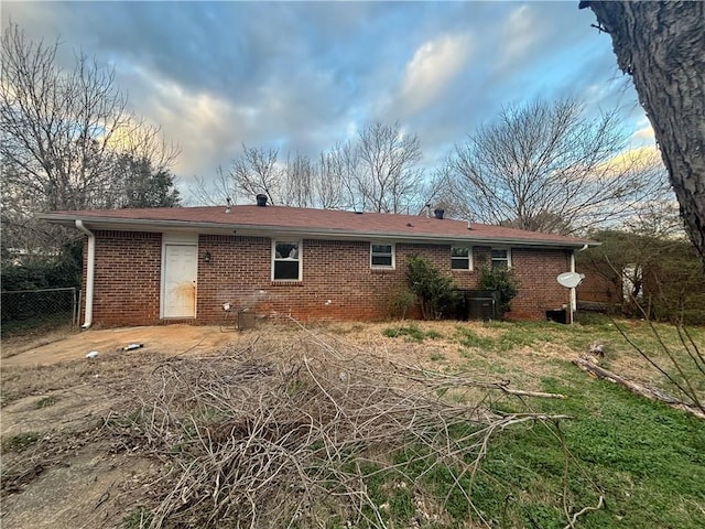 back of property with brick siding, central AC unit, and fence