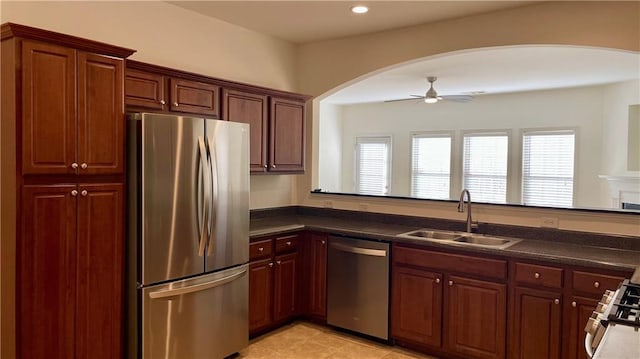 kitchen featuring appliances with stainless steel finishes, dark countertops, a sink, and ceiling fan