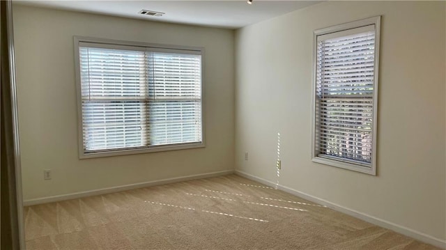 carpeted spare room with a healthy amount of sunlight, visible vents, and baseboards