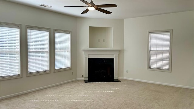 unfurnished living room featuring carpet flooring, visible vents, a fireplace with flush hearth, a ceiling fan, and plenty of natural light