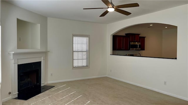 unfurnished living room featuring ceiling fan, a premium fireplace, light carpet, and baseboards