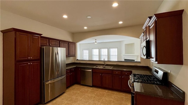 kitchen featuring arched walkways, a fireplace, recessed lighting, appliances with stainless steel finishes, and a sink