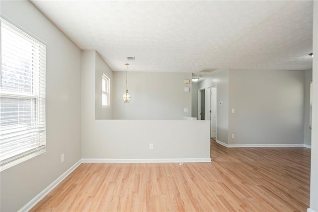 empty room featuring light wood-type flooring, baseboards, visible vents, and a textured ceiling