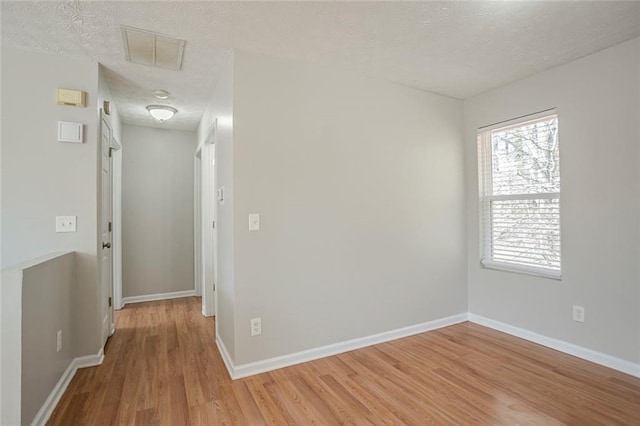 unfurnished room featuring a textured ceiling, light wood-type flooring, visible vents, and baseboards