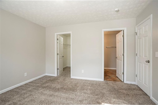 unfurnished bedroom with a spacious closet, a closet, carpet, and baseboards