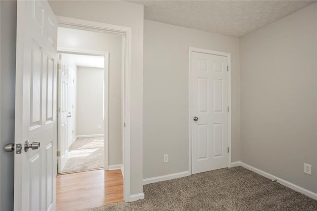 unfurnished bedroom featuring light wood-style floors, baseboards, a textured ceiling, and light colored carpet