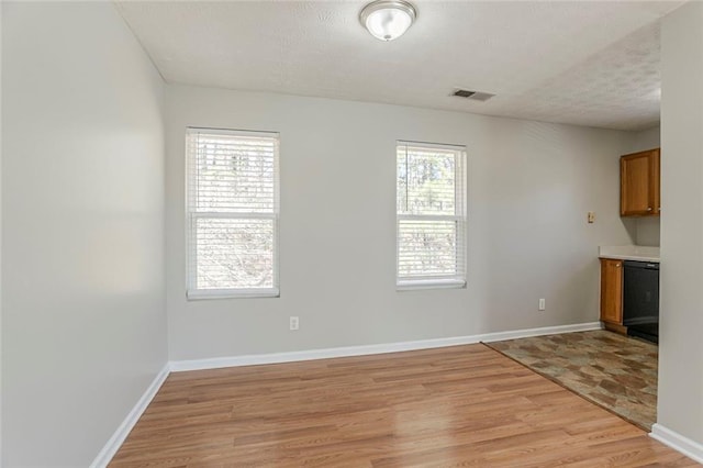 interior space with a textured ceiling, light wood-type flooring, visible vents, and baseboards