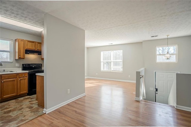 kitchen featuring brown cabinets, light countertops, light wood-type flooring, under cabinet range hood, and black / electric stove