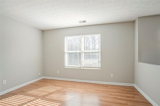 spare room with a textured ceiling, light wood finished floors, visible vents, and baseboards