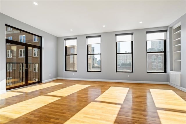 empty room with built in shelves, baseboards, and wood finished floors