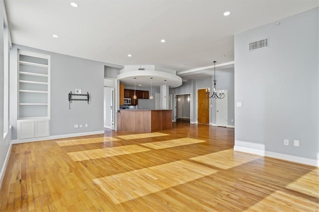 unfurnished living room with an inviting chandelier, built in features, baseboards, light wood-type flooring, and visible vents