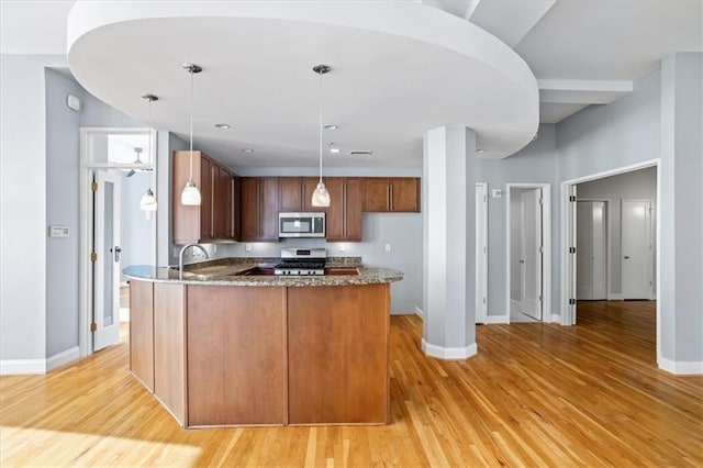 kitchen with baseboards, dark stone countertops, stainless steel appliances, and light wood-type flooring