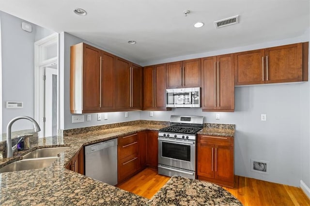 kitchen with stainless steel appliances, a sink, light wood-style flooring, and dark stone countertops
