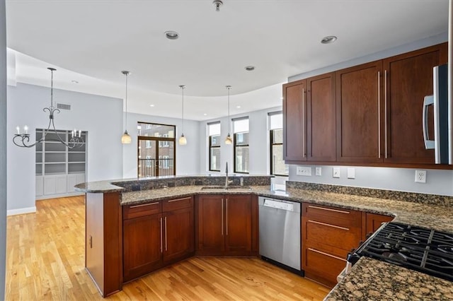 kitchen featuring a sink, light wood finished floors, appliances with stainless steel finishes, and dark stone counters