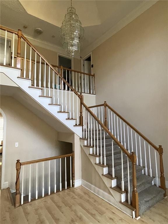 stairway with wood-type flooring, ornamental molding, and a chandelier