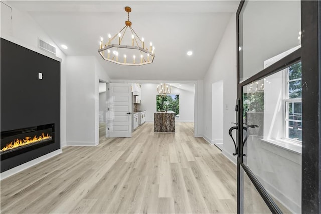 unfurnished living room featuring an inviting chandelier, a fireplace, vaulted ceiling, and light hardwood / wood-style floors