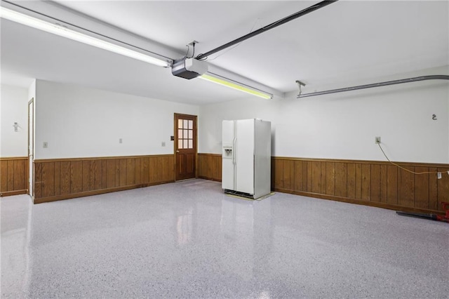 garage featuring a garage door opener, white refrigerator with ice dispenser, a wainscoted wall, and wood walls