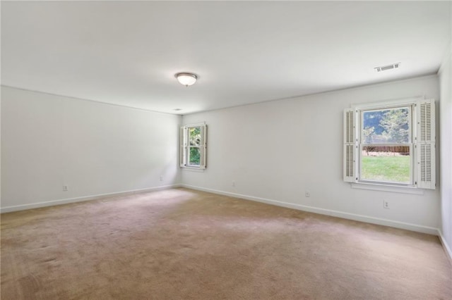 empty room featuring light carpet, visible vents, and baseboards