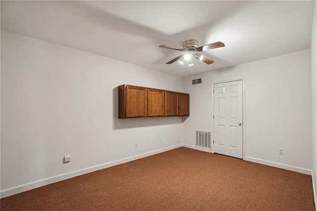 empty room featuring a ceiling fan, dark colored carpet, visible vents, and baseboards