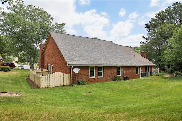 rear view of property featuring brick siding, a chimney, central air condition unit, a shingled roof, and a lawn