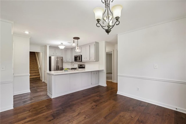 kitchen with dark wood finished floors, appliances with stainless steel finishes, a peninsula, light countertops, and a sink