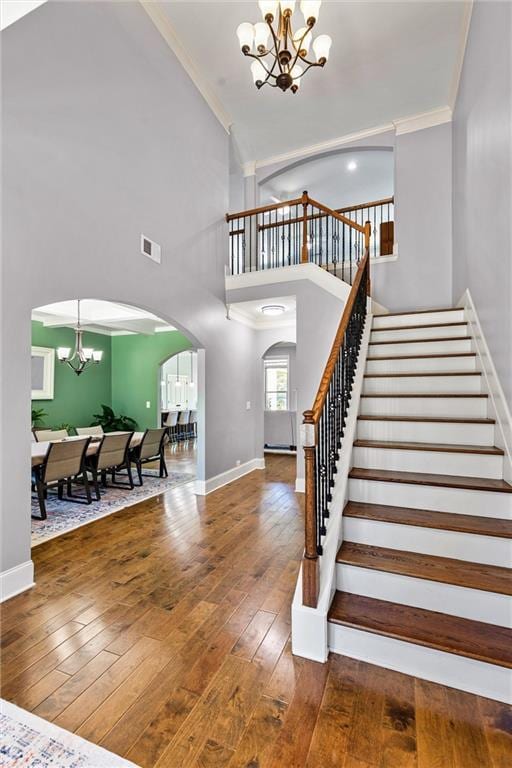 staircase featuring arched walkways, crown molding, a notable chandelier, wood-type flooring, and visible vents