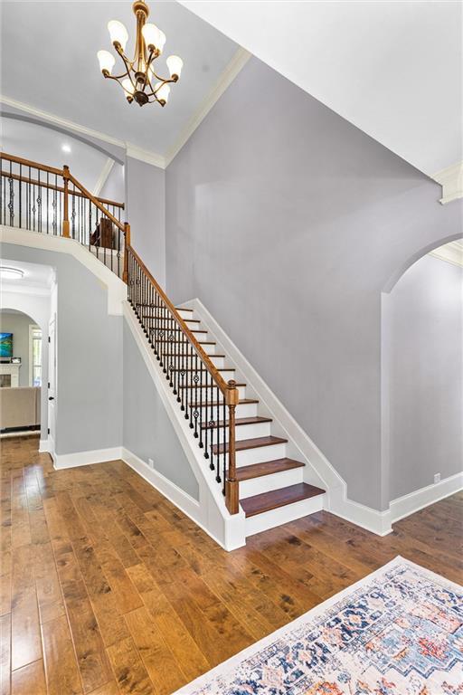 stairs with arched walkways, a towering ceiling, baseboards, ornamental molding, and wood-type flooring