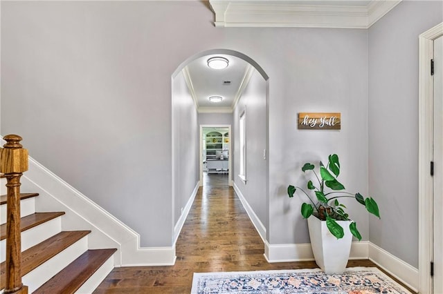 hallway featuring arched walkways, baseboards, wood finished floors, and crown molding