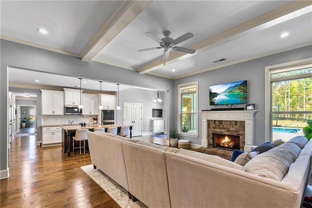 living room featuring baseboards, ornamental molding, dark wood-type flooring, a brick fireplace, and beam ceiling