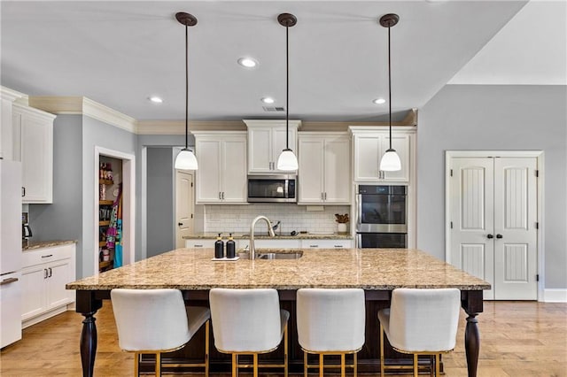 kitchen featuring light stone counters, stainless steel appliances, white cabinetry, hanging light fixtures, and a center island with sink