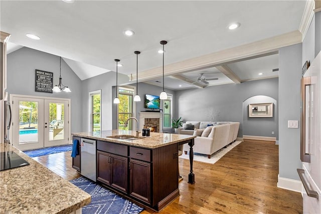 kitchen with dark brown cabinetry, a center island with sink, a sink, a fireplace, and stainless steel dishwasher