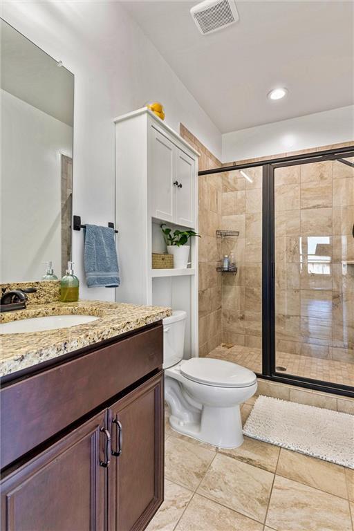 full bath with toilet, vanity, a shower stall, and visible vents