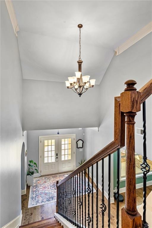 stairs featuring arched walkways, french doors, a notable chandelier, vaulted ceiling, and wood finished floors