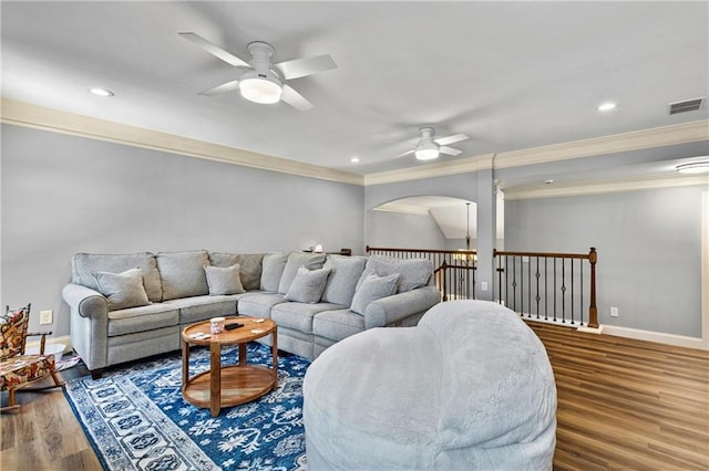 living room with dark wood-style flooring, a ceiling fan, visible vents, baseboards, and ornamental molding