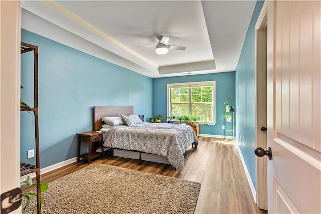 bedroom featuring a ceiling fan, a raised ceiling, baseboards, and wood finished floors